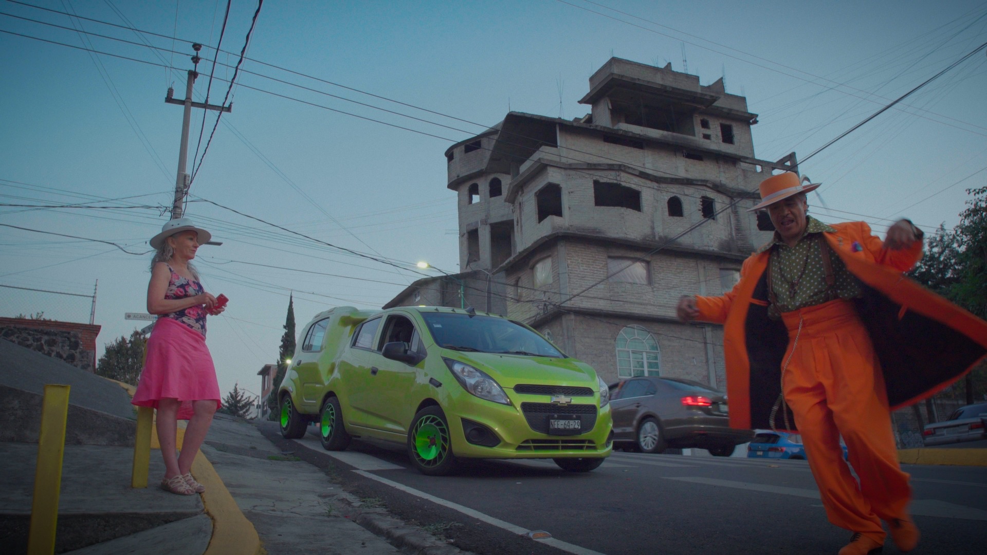 Fotograma de El Cumbé: un pachuco vestido de naranja baila junto a un automóvil verde